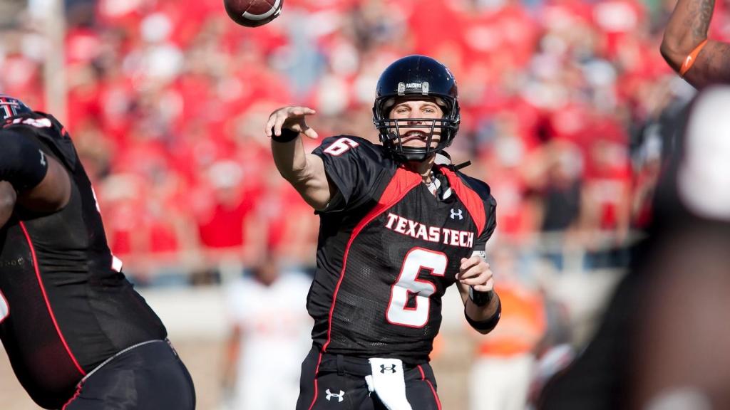 Action shot of Texas Tech quarterback Graham Harrell in a black and red Under Armour jersey with the number 6, mid-throw during a football game with a blurred crowd in the background.