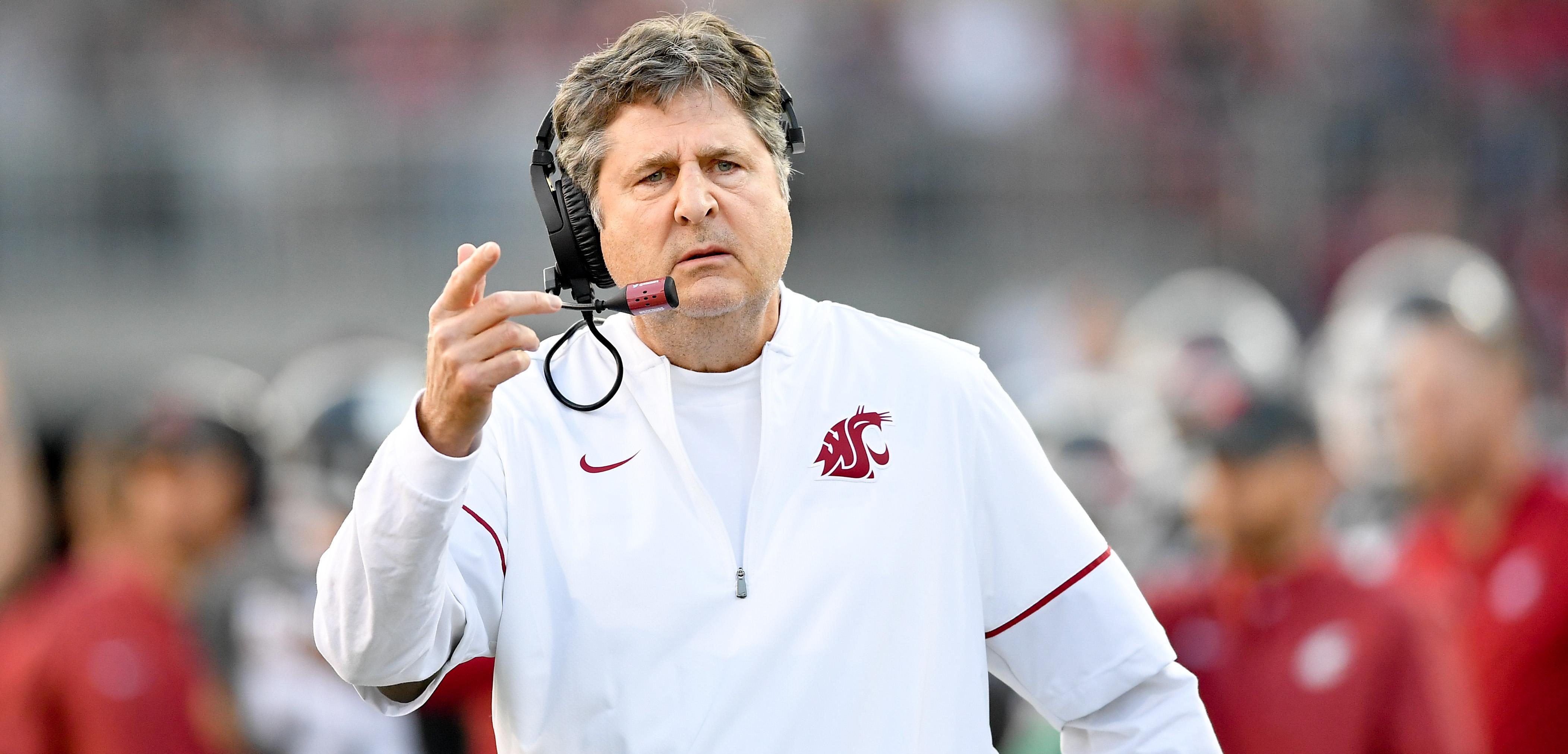 Washington State head coach Mike Leach on the sideline wearing a white team pullover and headset, pointing and looking intensely during a game.